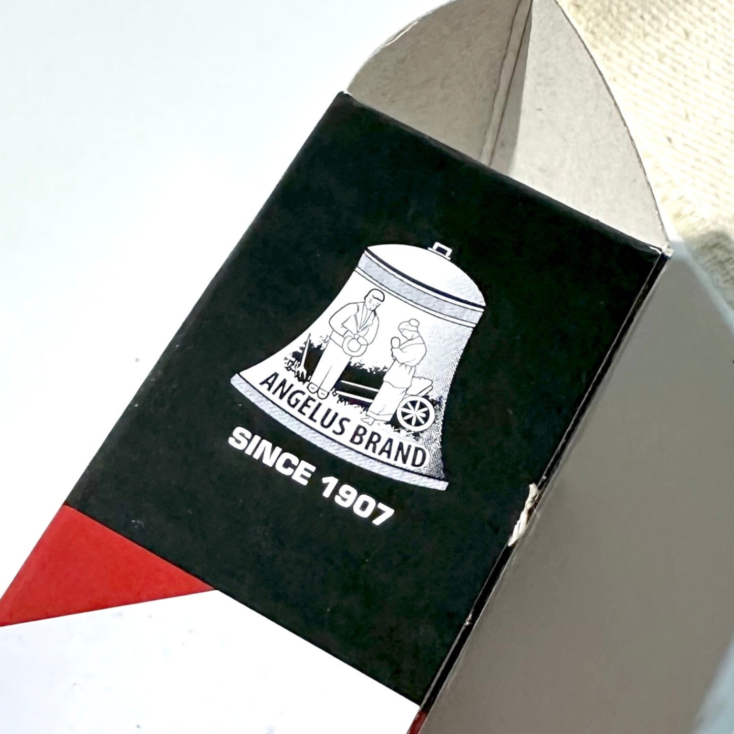 Angelus shoe care logo, branded box on a red and white striped background.