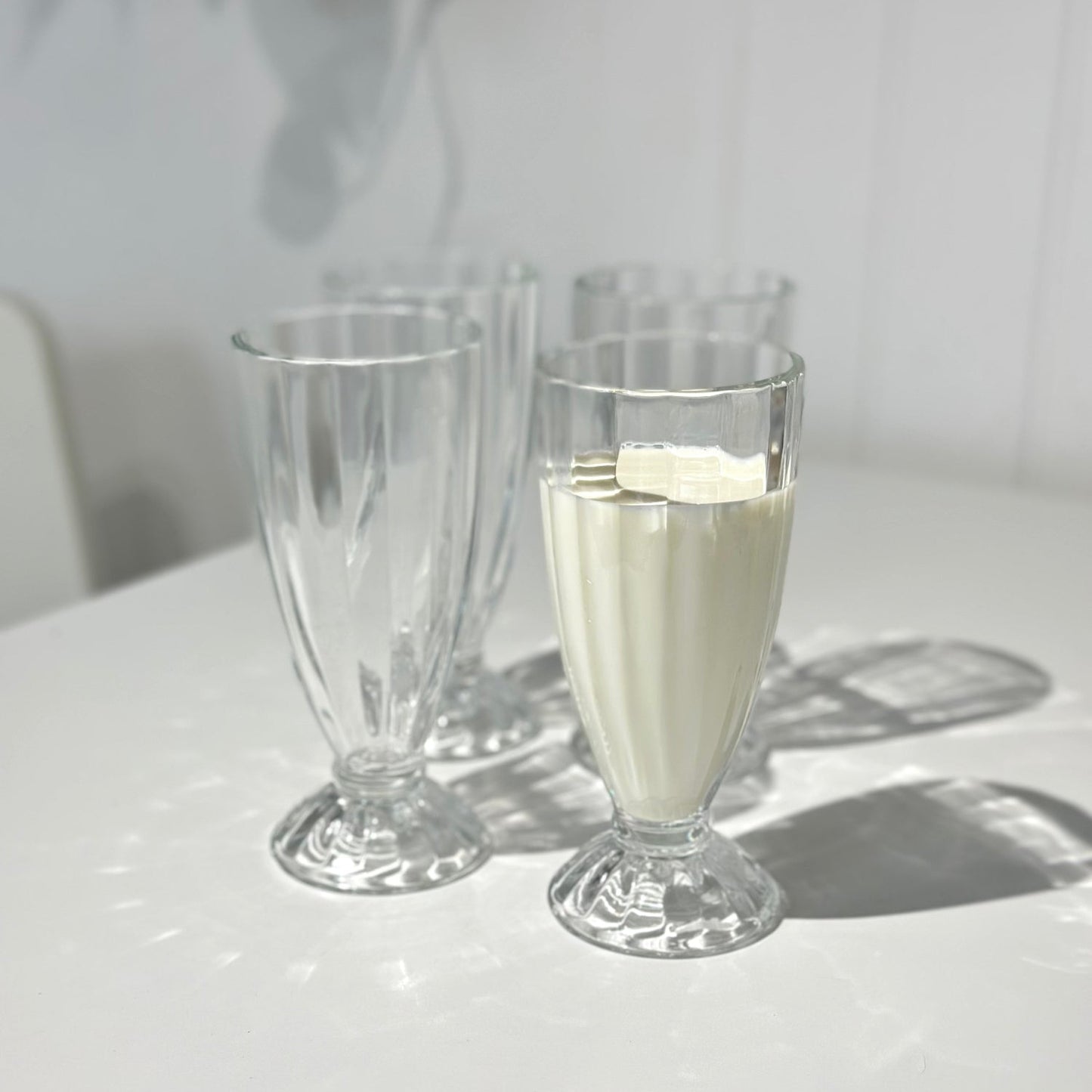 Two clear glasses on a white surface with one containing a white liquid.
