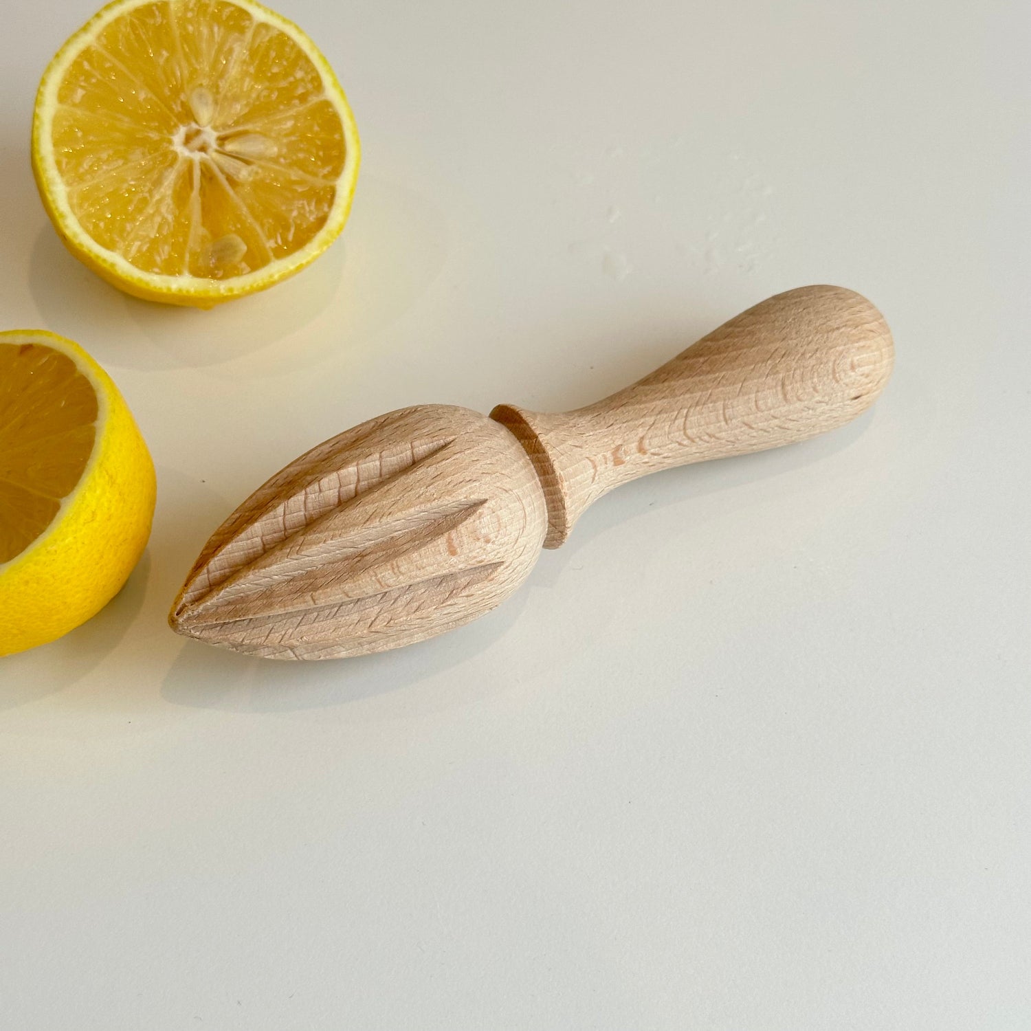 Wooden lemon squeezer with two lemons on a light background