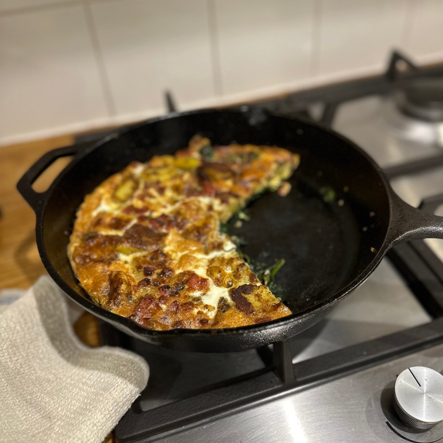 Frittata in a cast iron skillet on a gas stove with a white tiled wall background