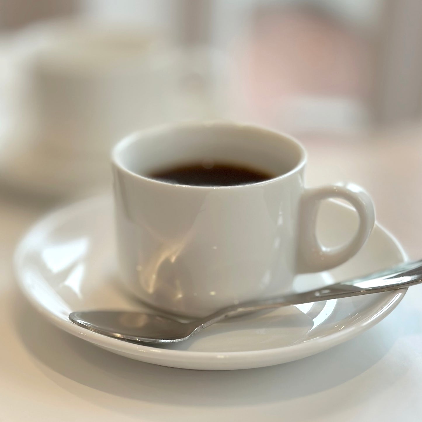 White coffee cup with a spoon on a saucer on a light surface