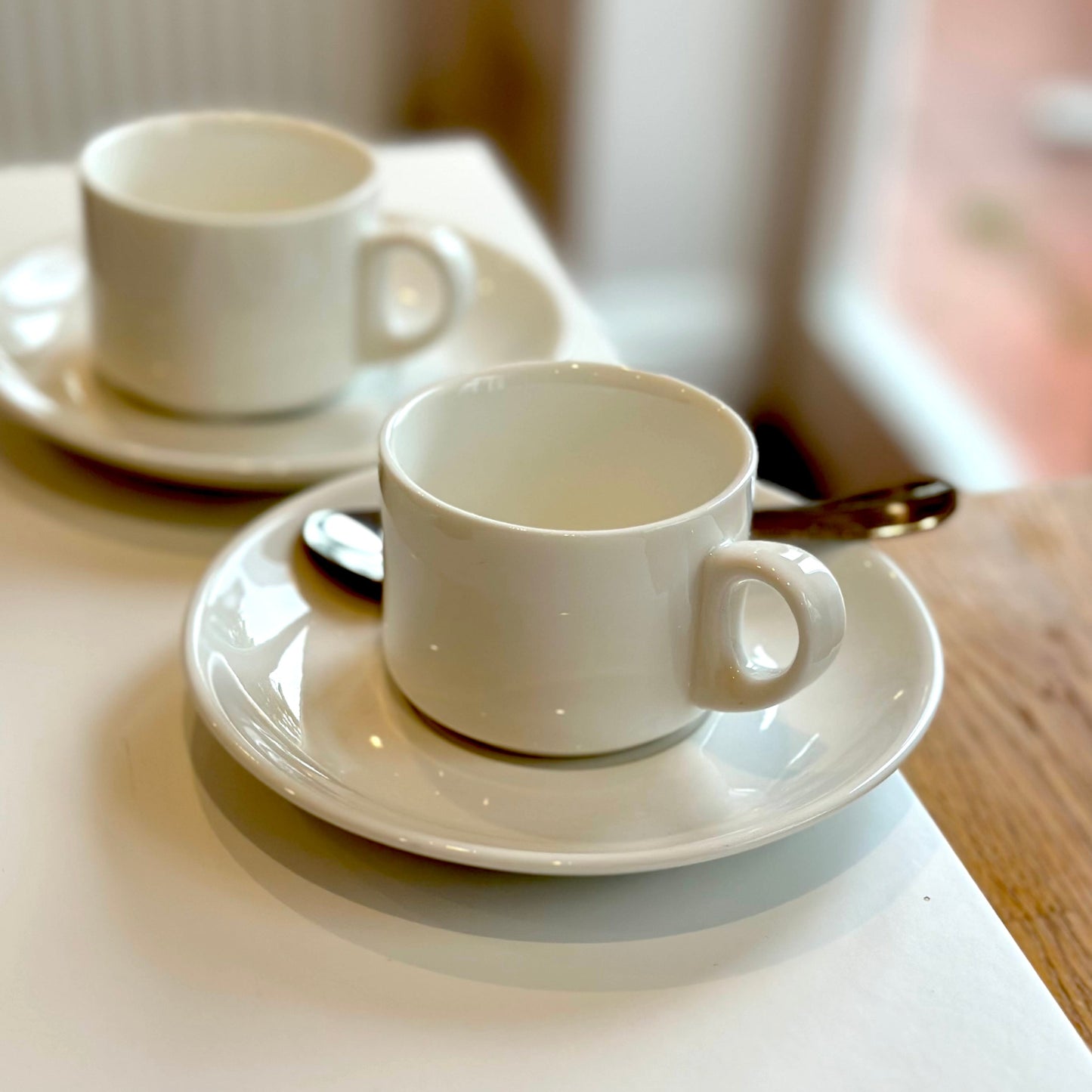 Pair of white espresso cups and saucers on a white counter