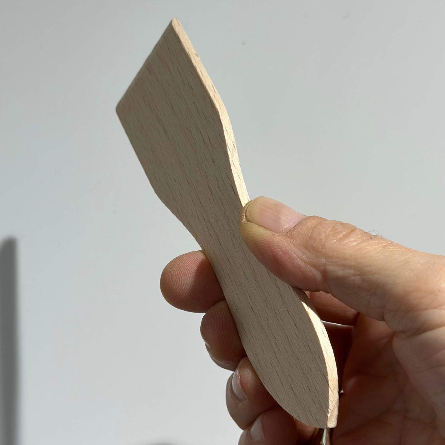 Hand holding a small wooden object against a plain background