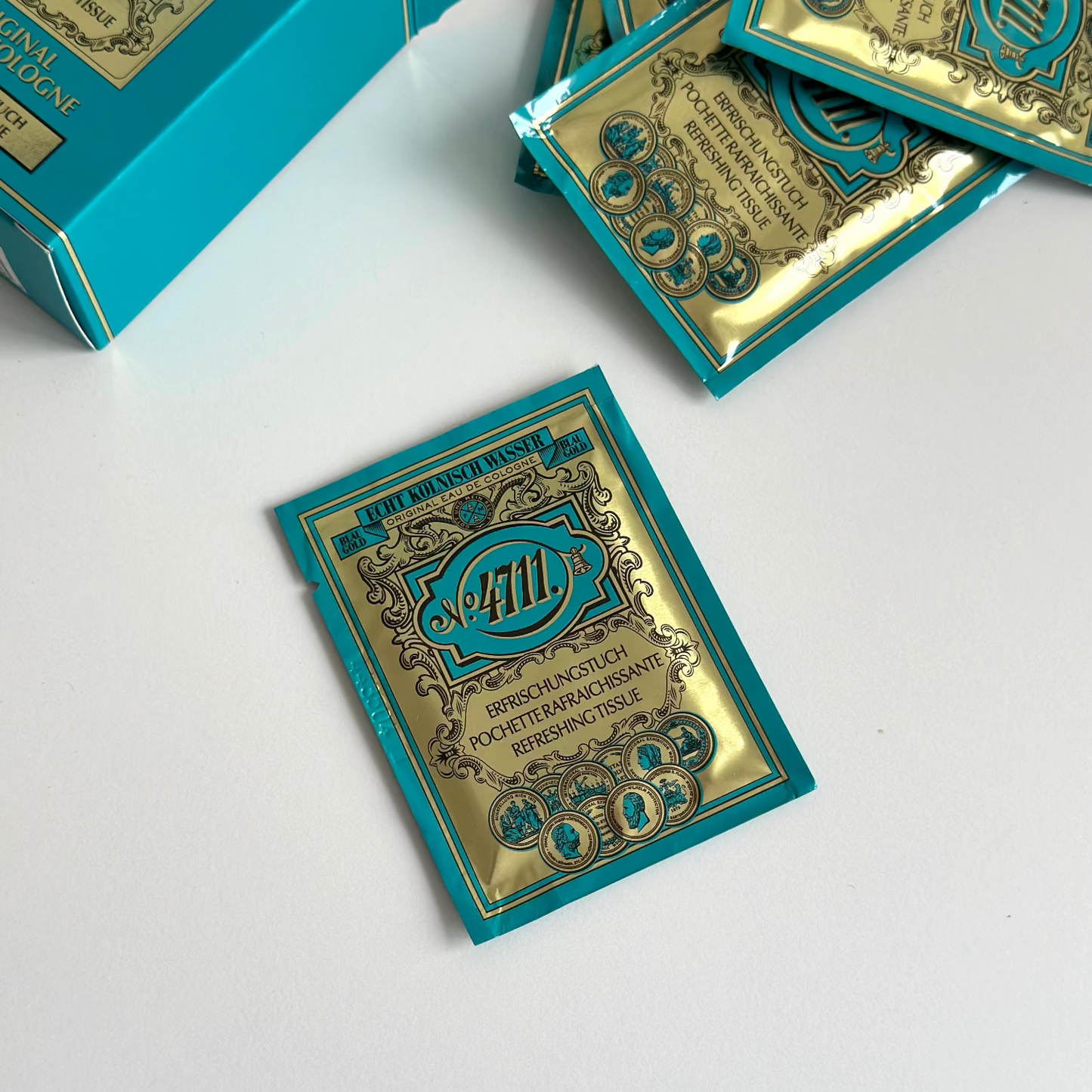 Turquoise and gold cosmetic sachets and an open matching box arranged on a white surface. The packaging features ornate decorative borders and a central crest with the number 411.