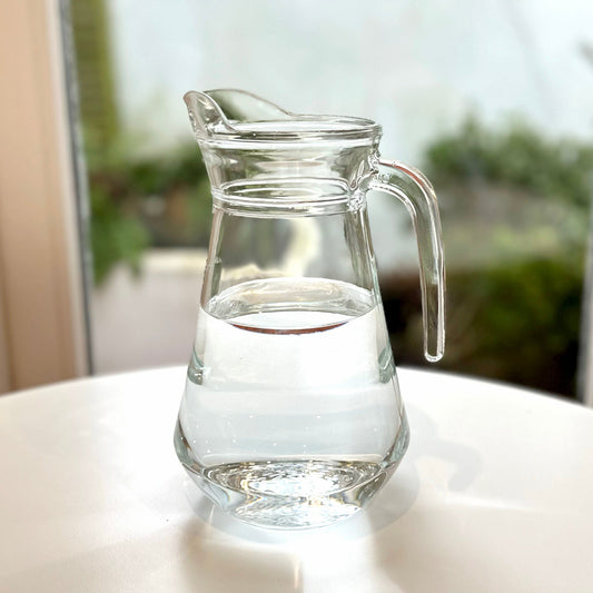 Arc glass water jug with water against a window