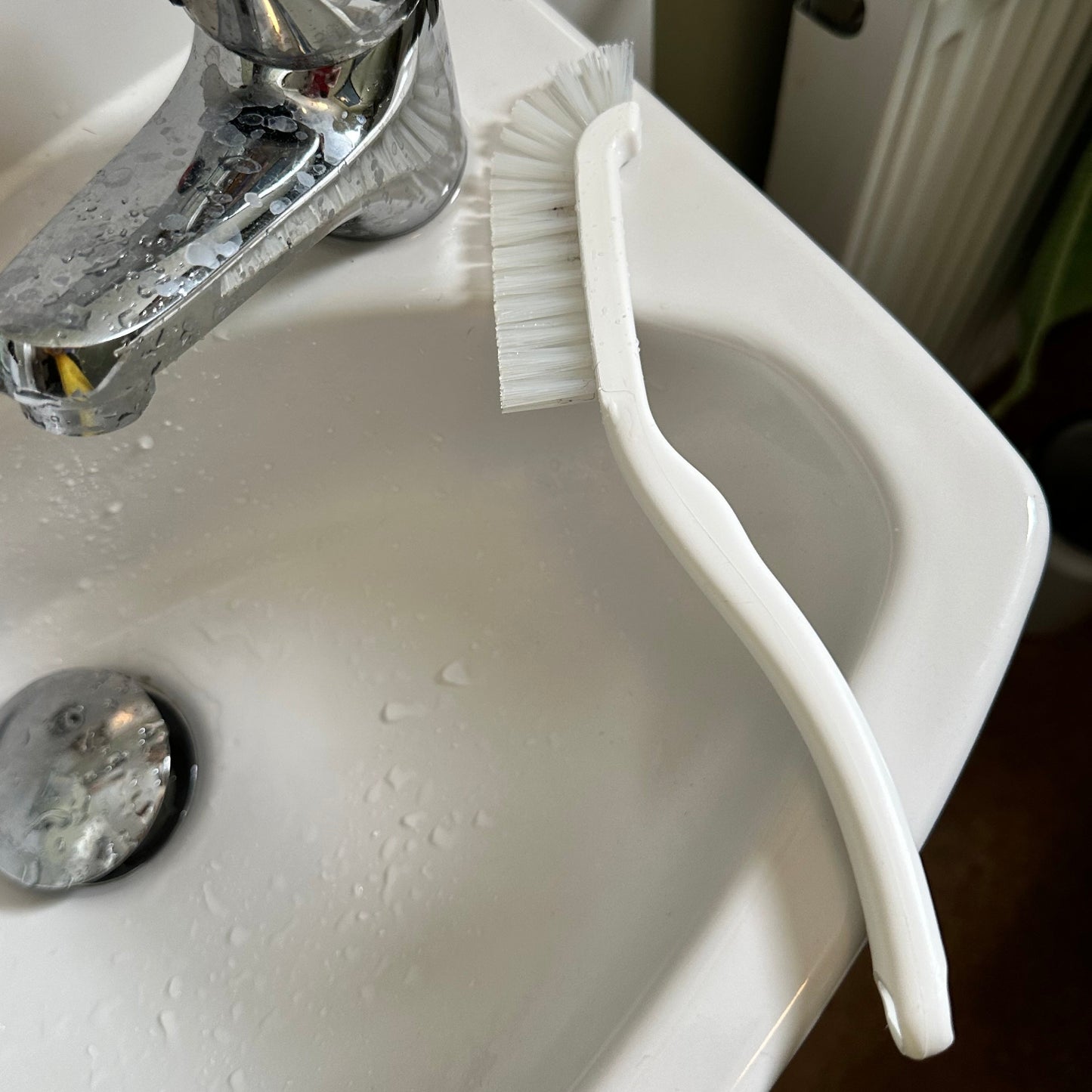White sink with a tap and a white brush leaning against it.