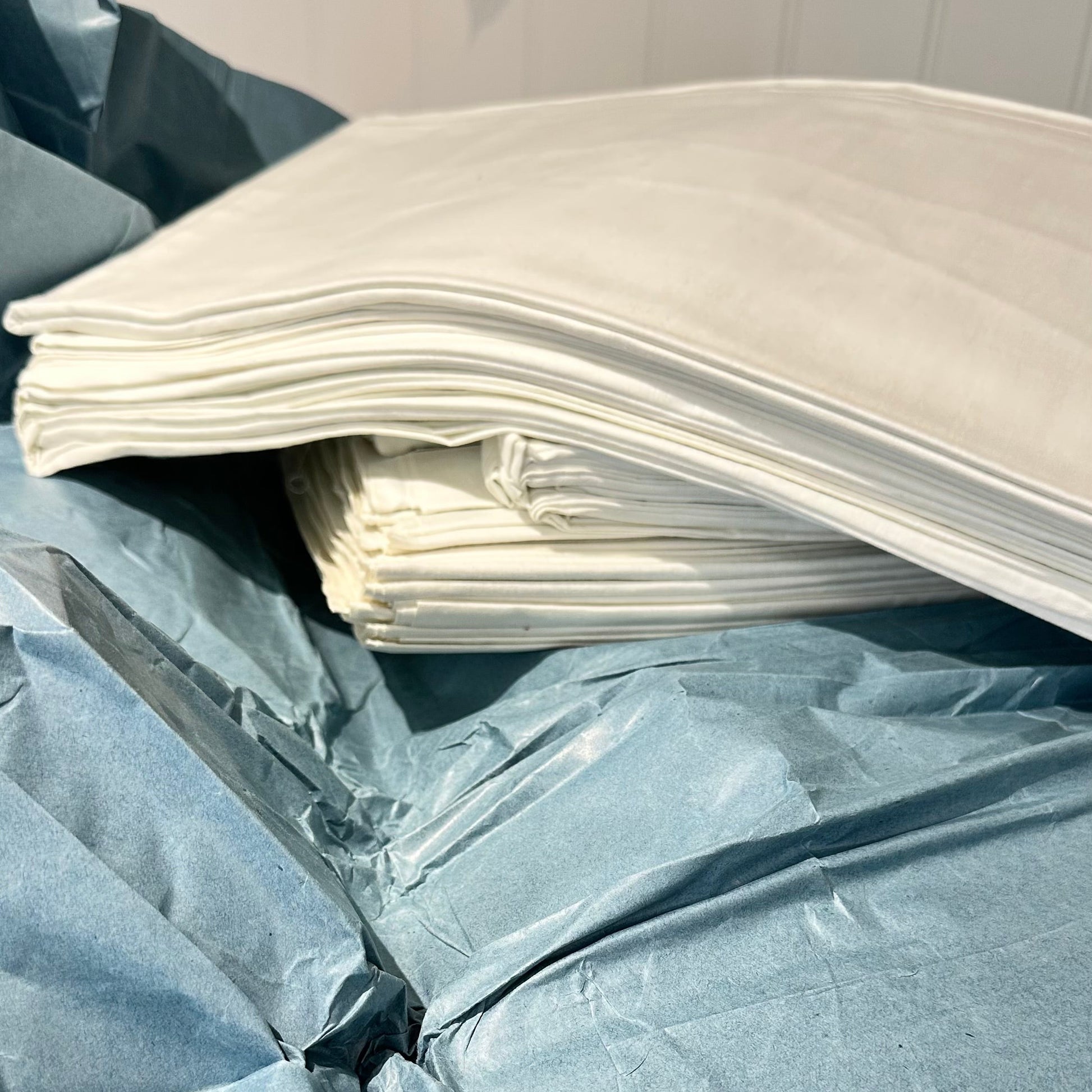 A stack of white rectangular fabric or paper sheets resting on top of crumpled light blue material, photographed in a close-up indoor shot.