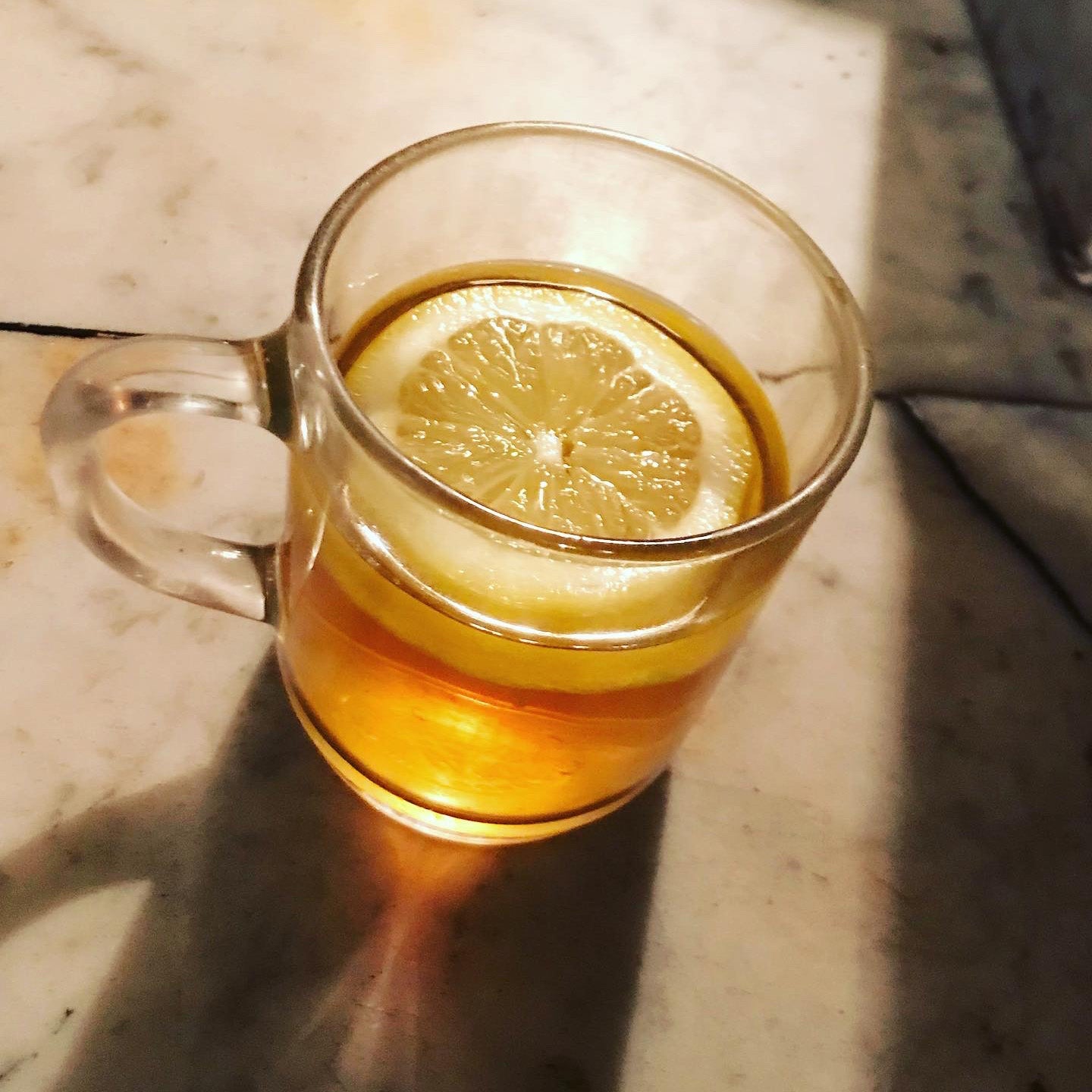 Clear glass mug with lemon slice on a marble surface