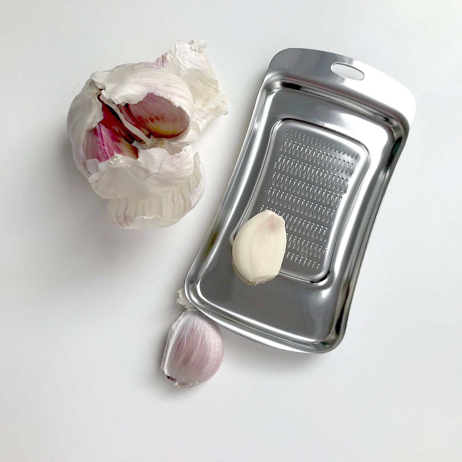 Stainless steel garlic peeler with a peeled garlic clove on a white background
