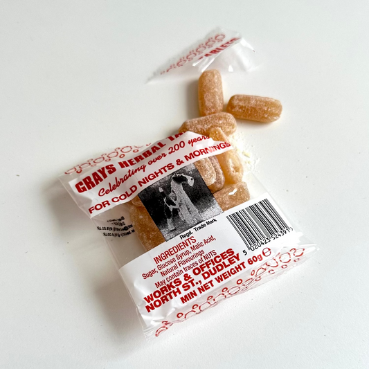 A small clear plastic packet of Grays Herbal tablets with three orange-brown mints visible, photographed on a plain white background.