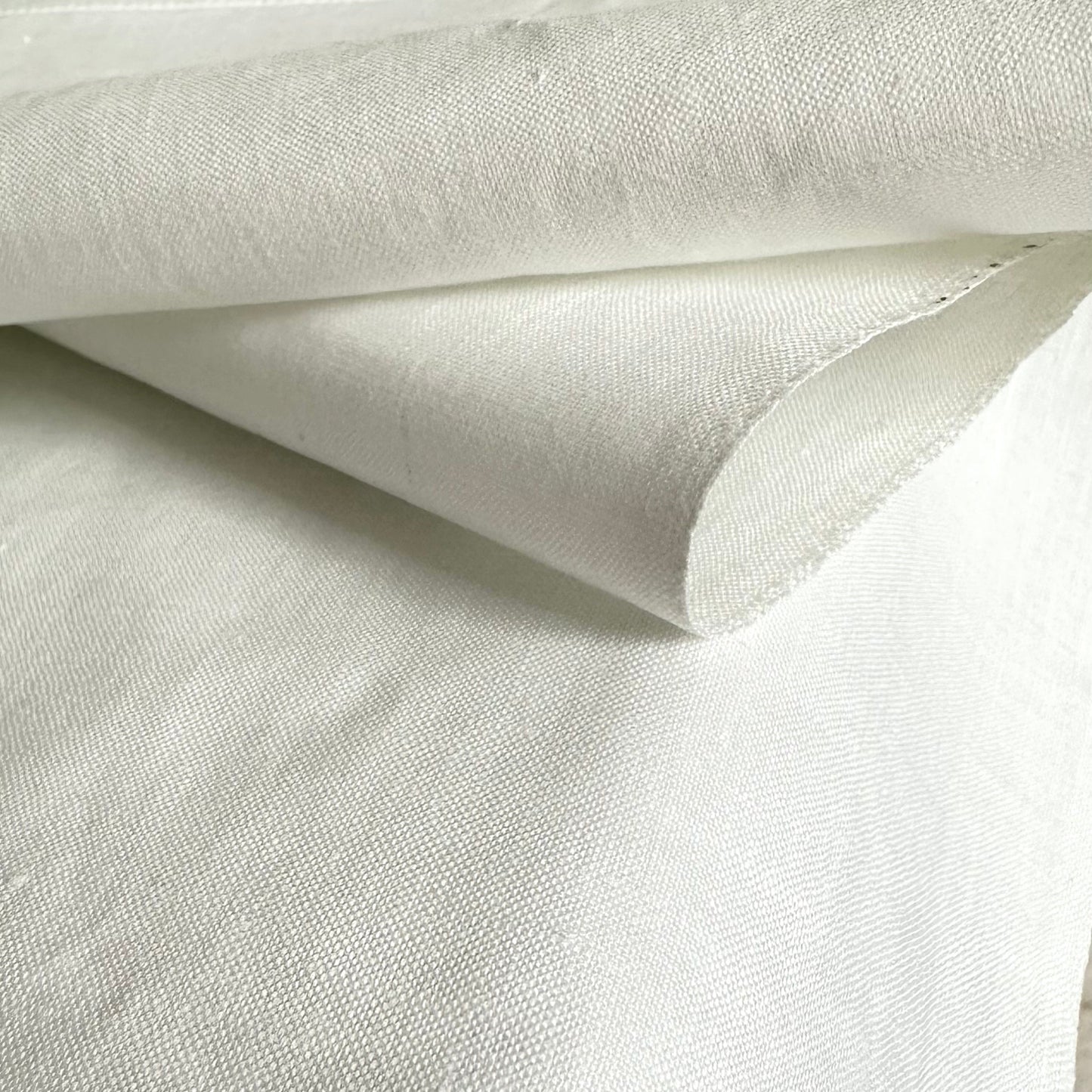 A close-up of white textured fabric, a white  cotton tablecloth folded over to show its weave and hem detail.