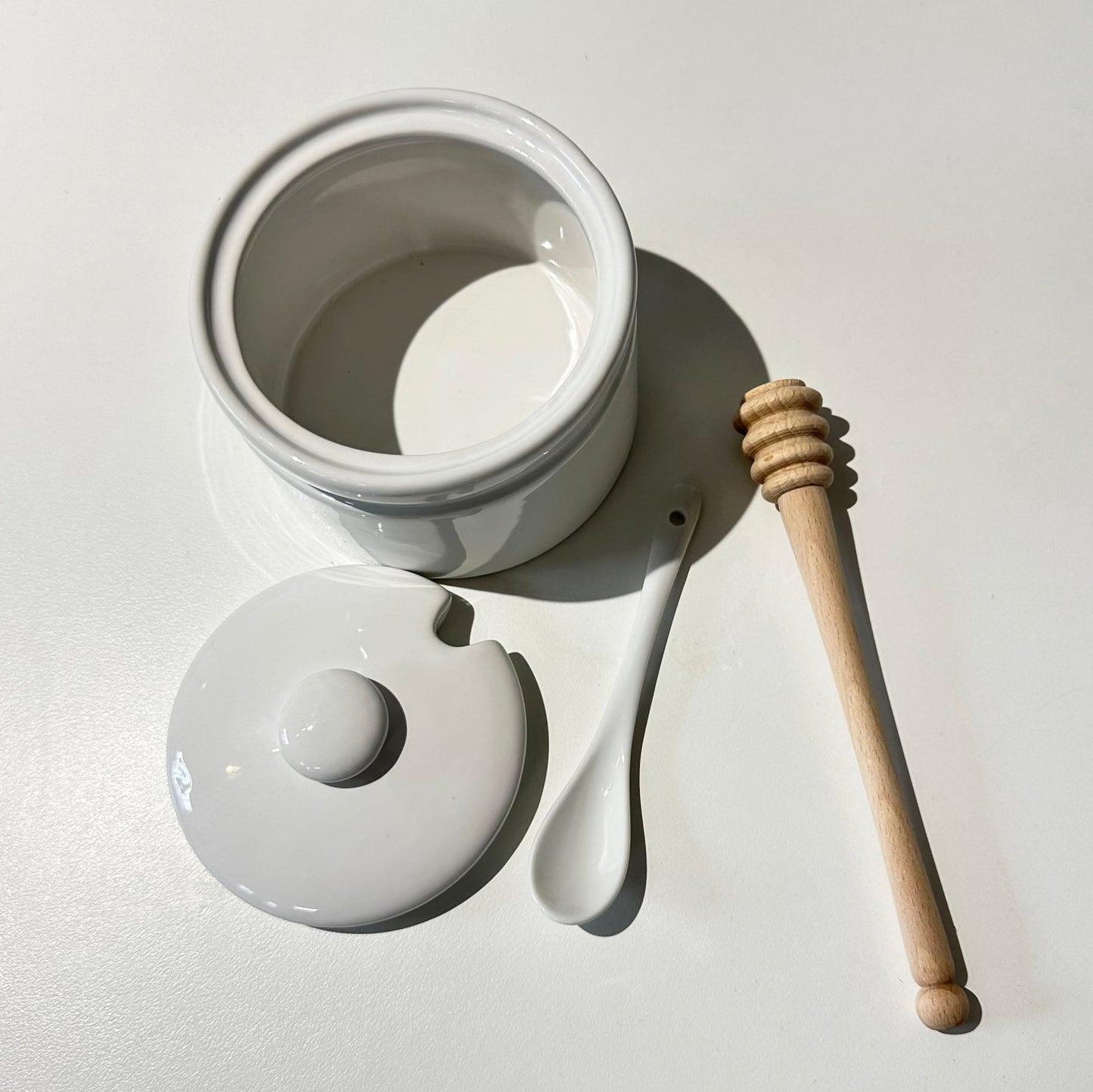 White ceramic jar with a wooden honey dipper on a light gray background