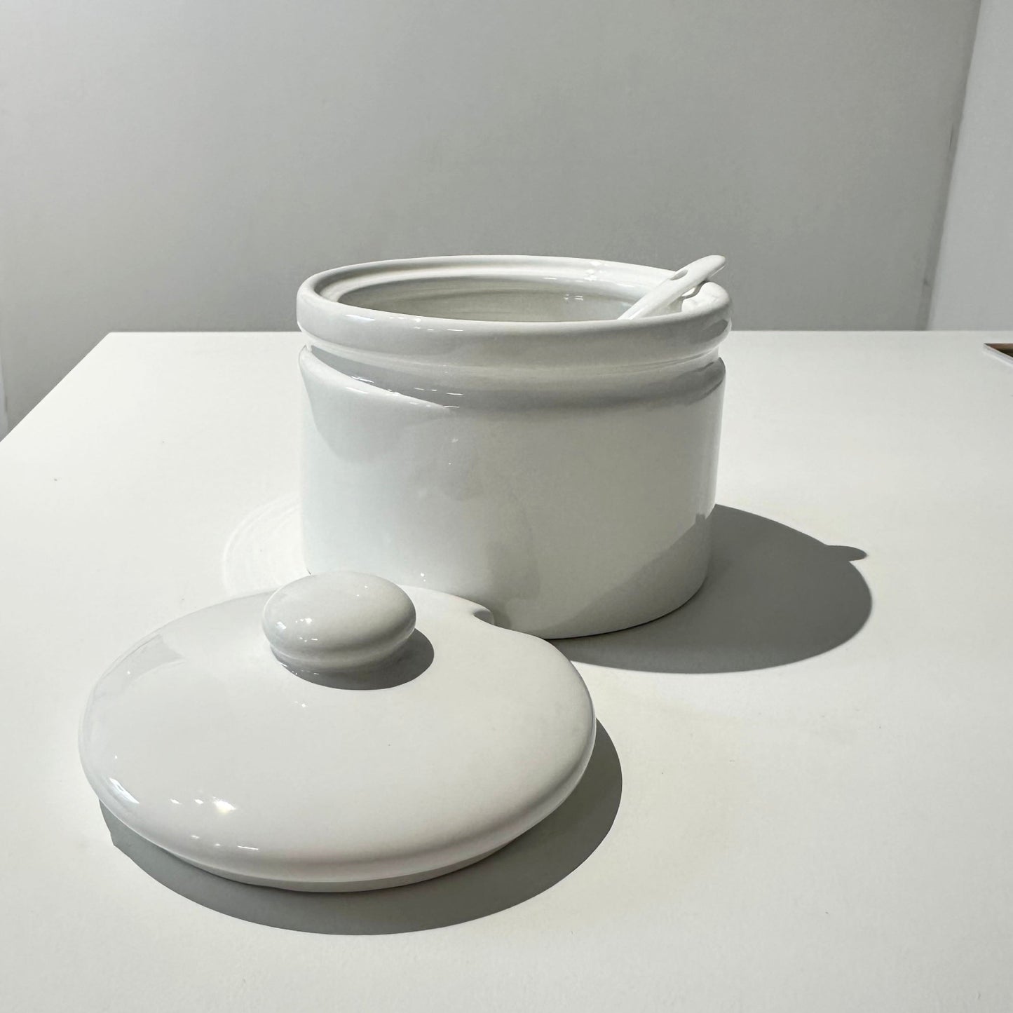 White ceramic jar with a lid on a light gray surface