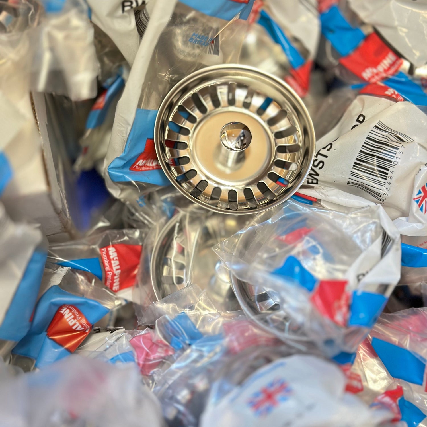 Metal sink strainer surrounded by plastic packaging with visible brand logo.