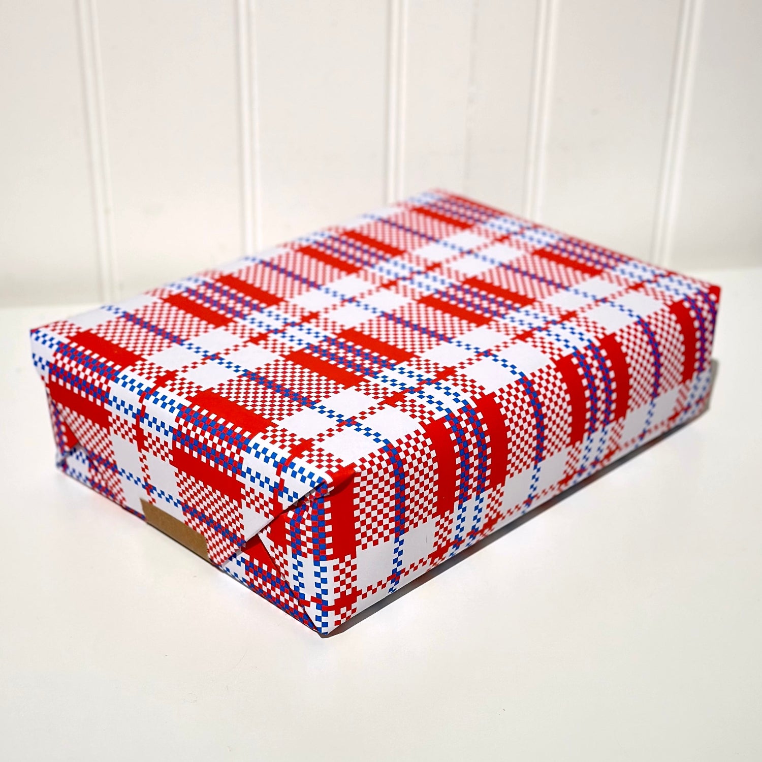 Present wrapped with red, white, and blue plaid pattern gift wrap on a white surface.