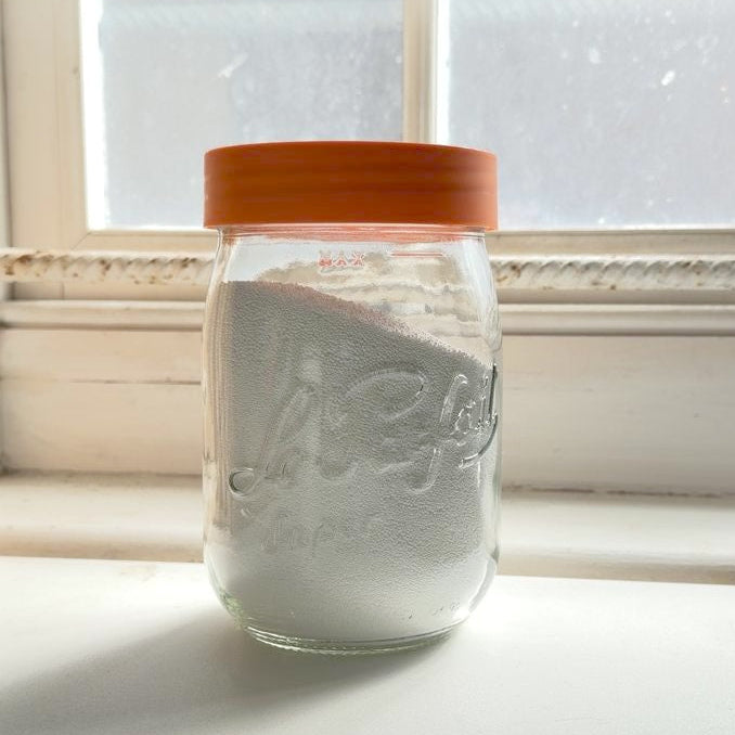 Le Parfait jar with an orange lid with detergent against a window