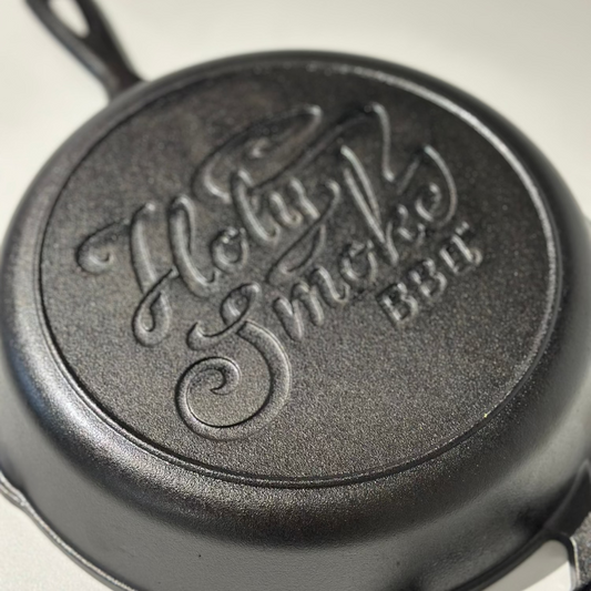 Cast iron skillet with 'Holly Smoke BBQ' branding on a light gray background