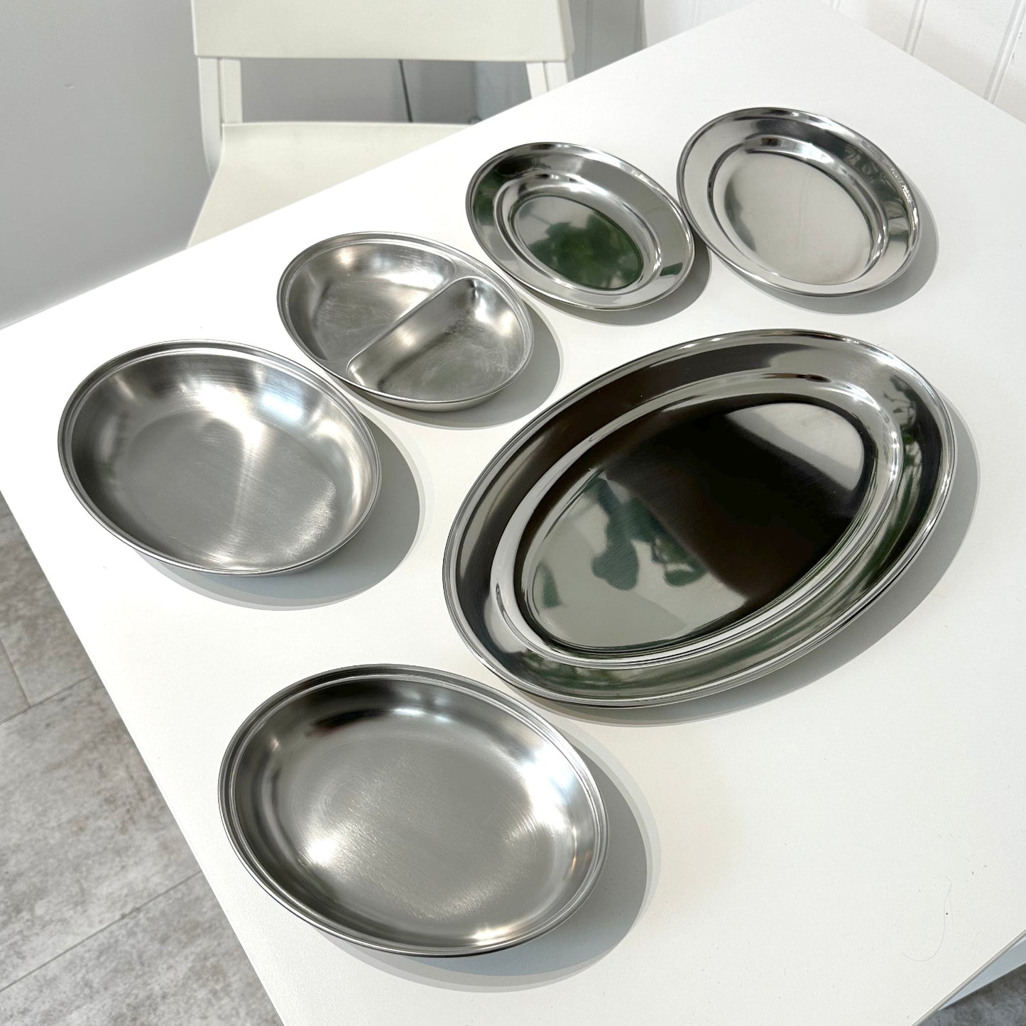 Selection of stainless steel meat flat dishes on a white table