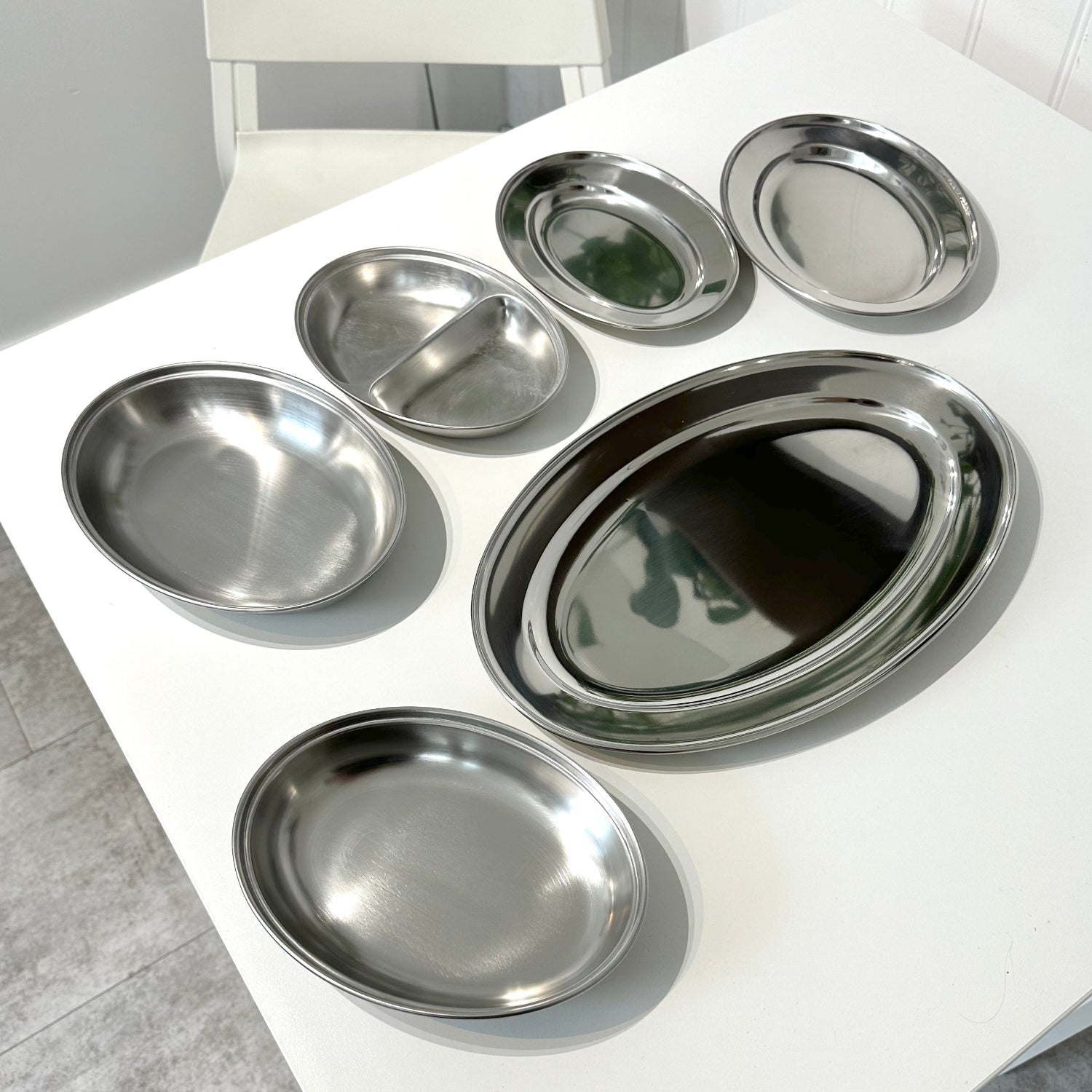 Selection of stainless steel meat flat dishes on a white table