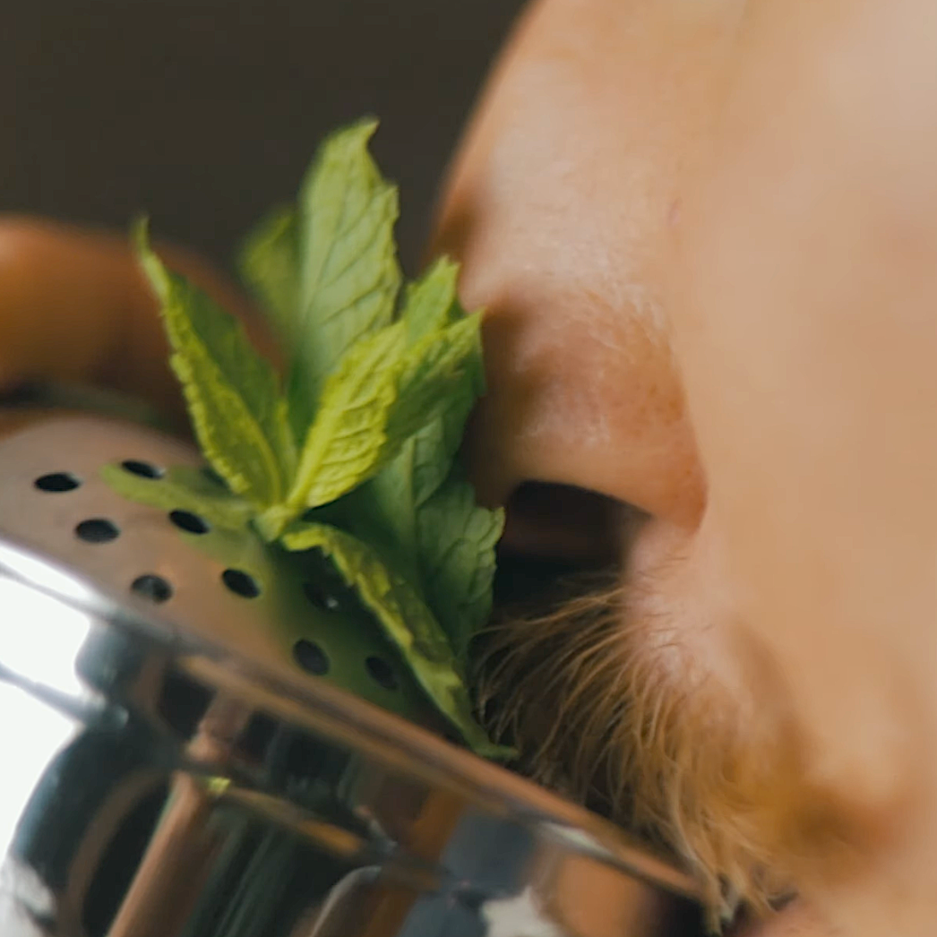 Close-up of a person using a metal strainer with mint leaves over a dark background