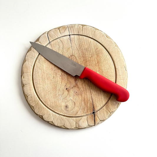 Wooden cutting board with a red-handled knife on a white background