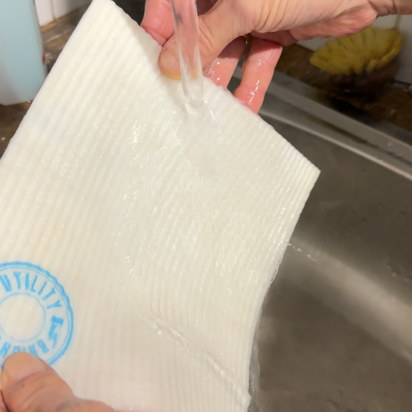 Clean white dish cloth being rinsed under tap