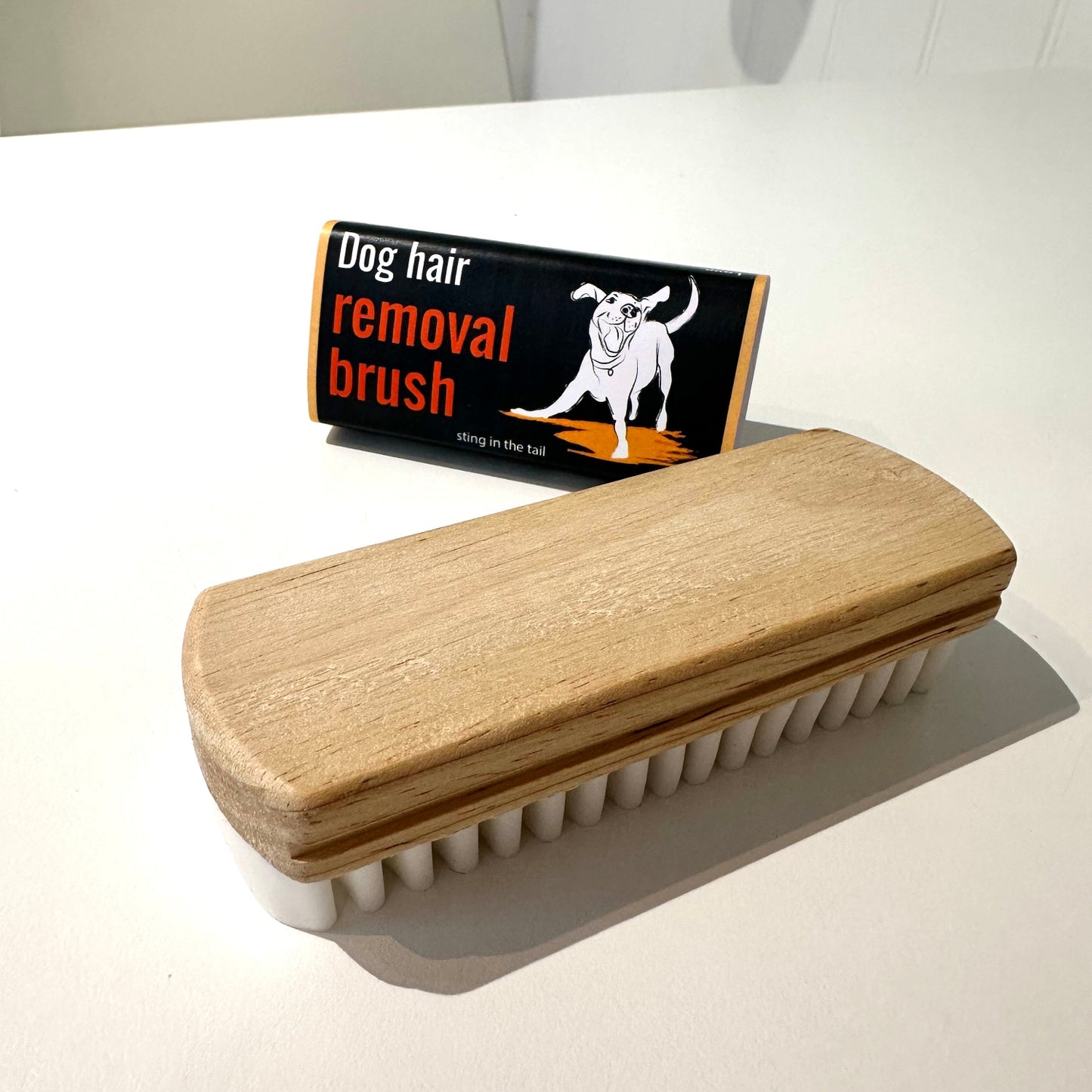 Dog hair removal brush with wooden handle and white bristles on a white surface.