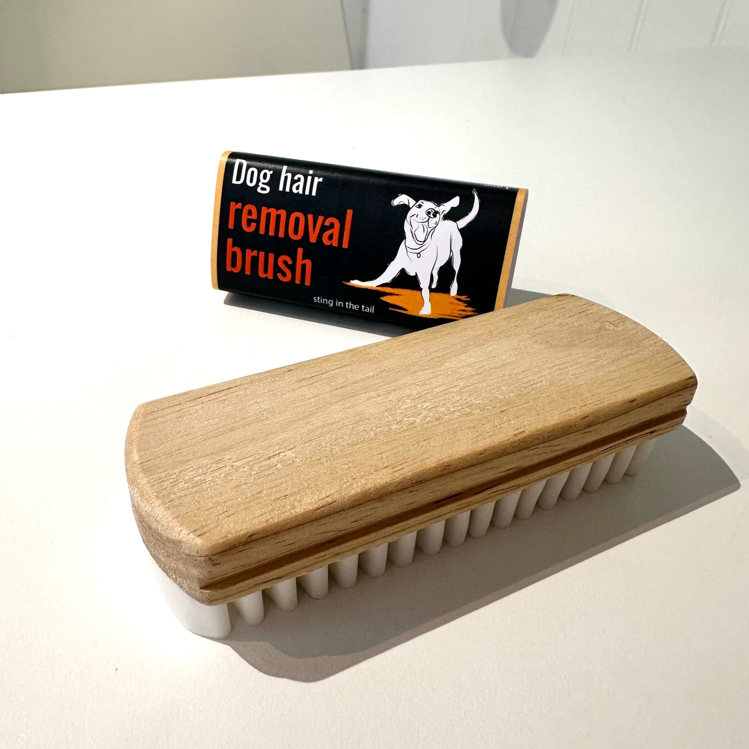 Dog hair removal brush with wooden handle and white bristles on a white surface.