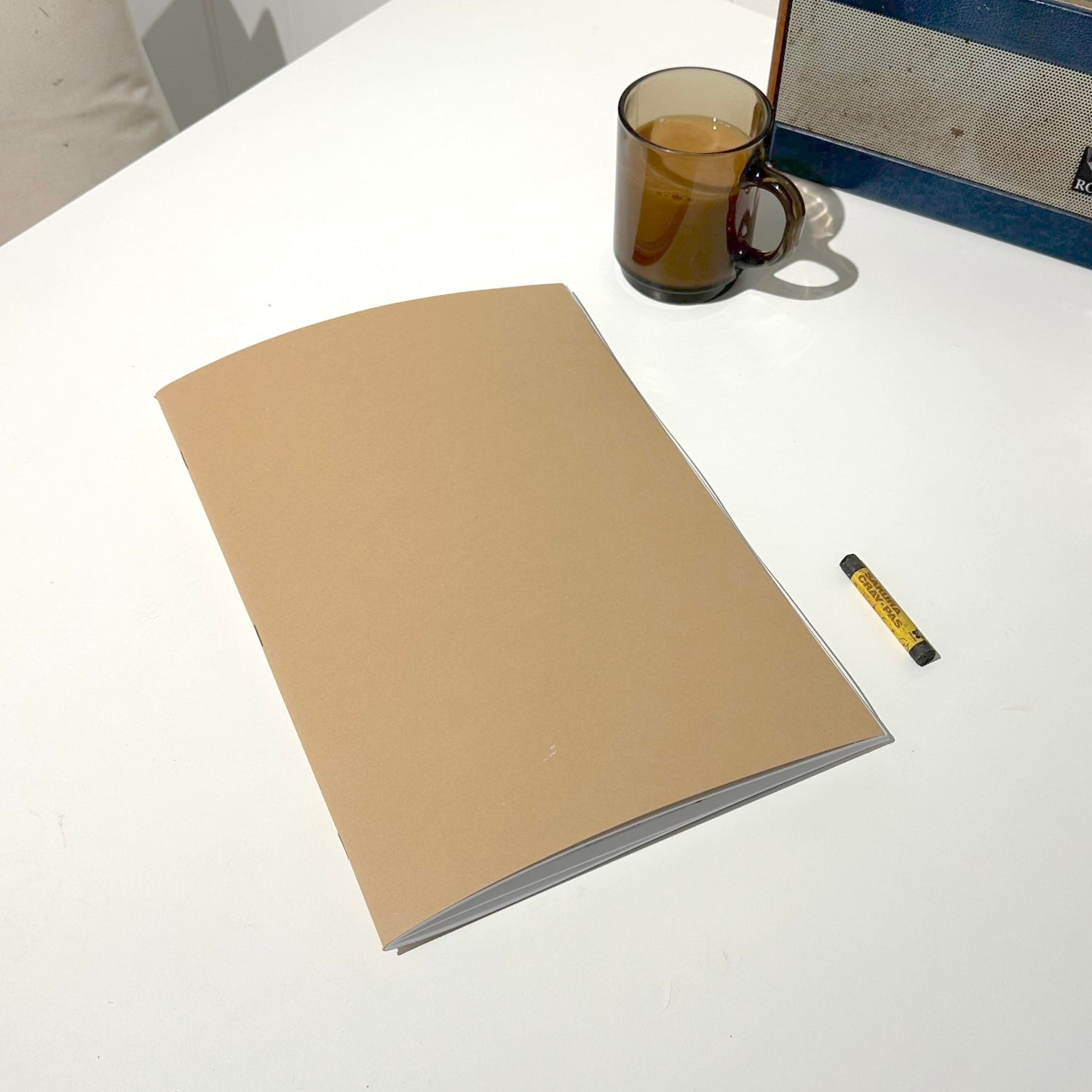 Beige notebook on a white table with a glass mug and radio in the background