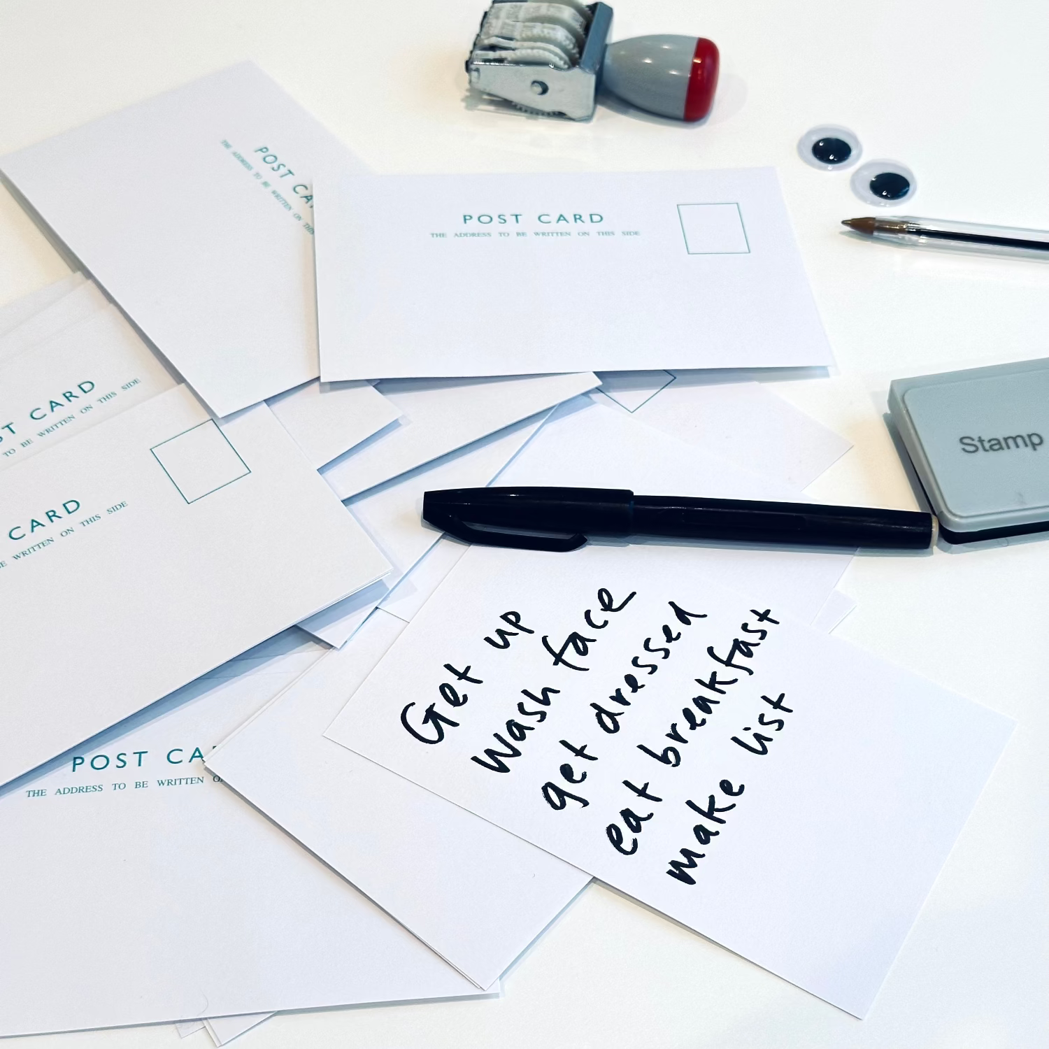 Postcards with handwritten text, a pen, and stamps on a white surface