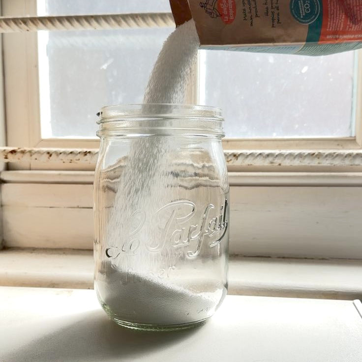 White detergent pouring into a glass jar against a window