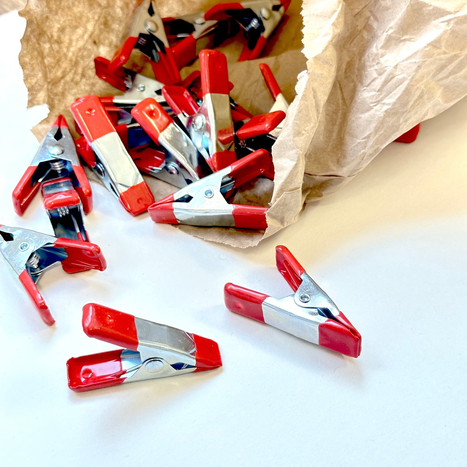 Red and silver clips scattered on a white surface with a brown paper bag in the background.
