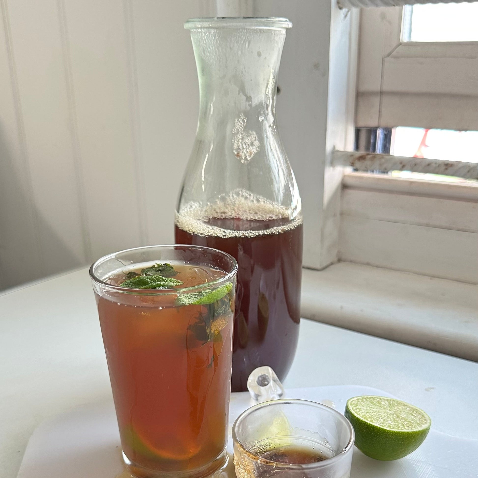 Two glasses of iced tea with a carafe on a white surface.