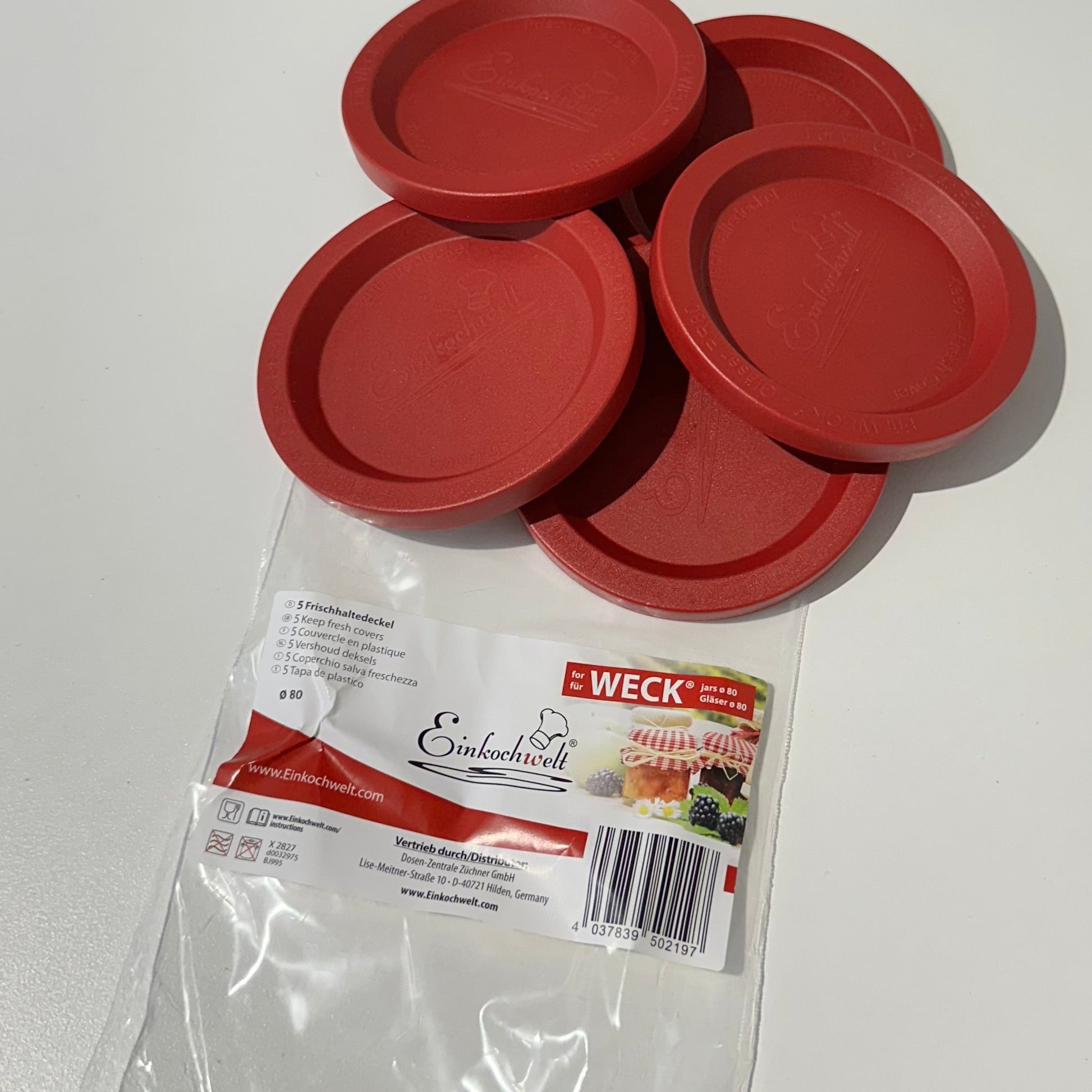 Red Weck jar lids on a white surface with a clear plastic bag underneath.