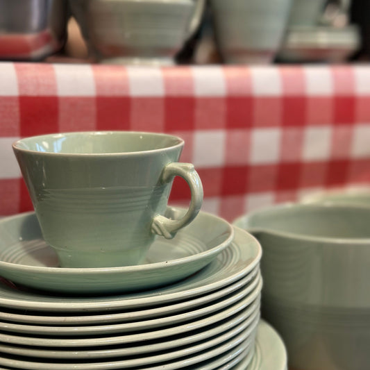 Stack of green ceramic cups and saucers on a red and white checkered tablecloth.
