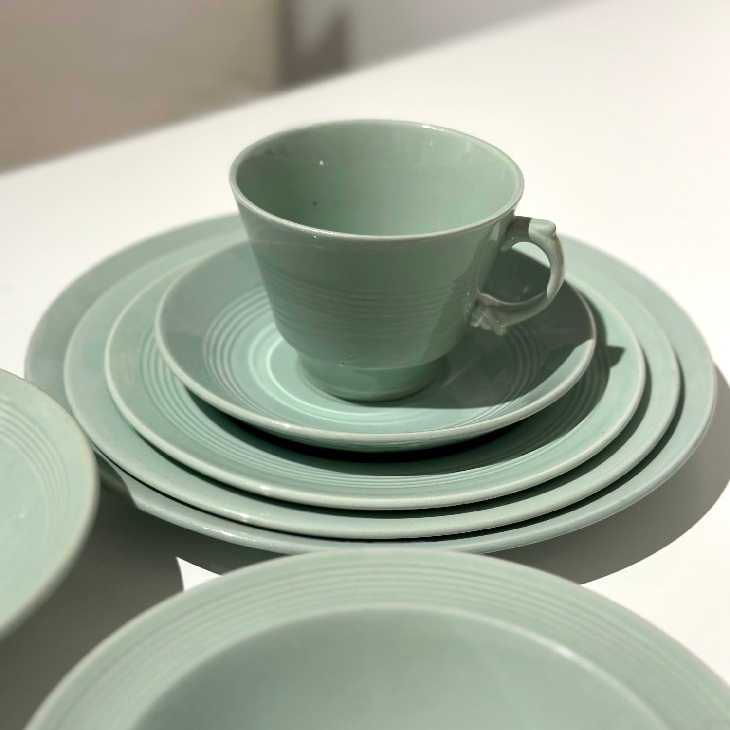 Set of green ceramic dishes including a cup, saucer, and bowls on a white surface.