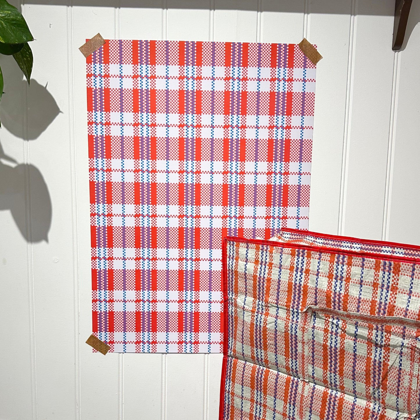 Red and blue plaid fabric on a white wall with a plant in the corner.