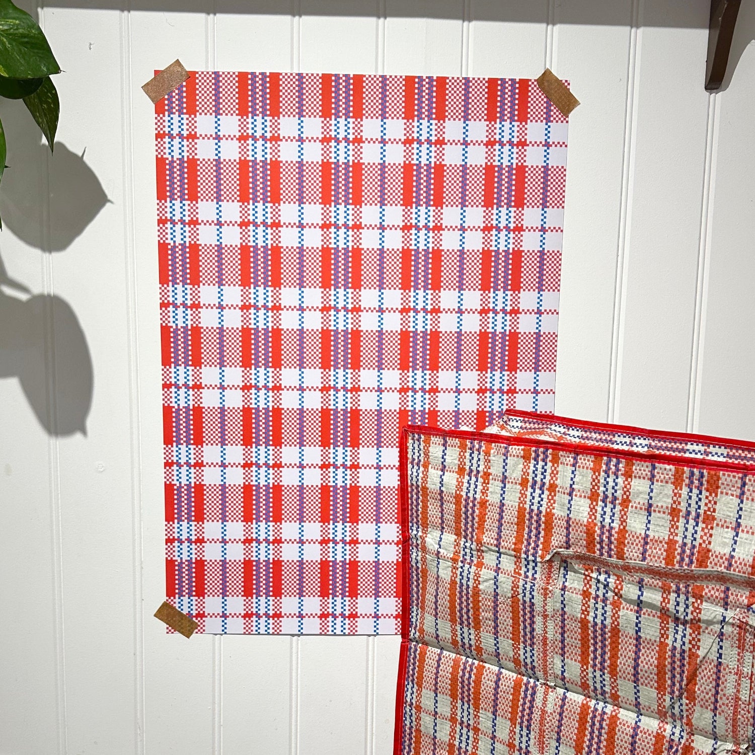 Red and blue plaid fabric on a white wall with a plant in the corner.
