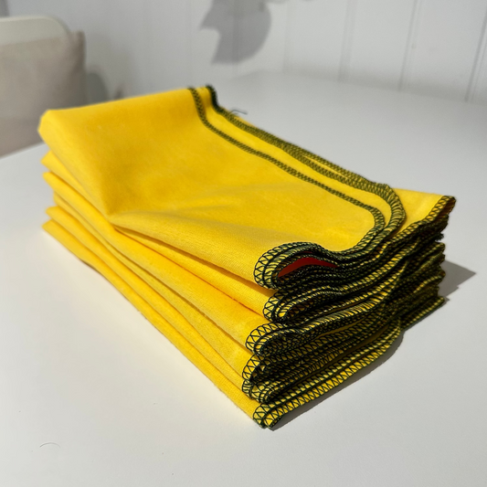 A stack of yellow dusters with green overlocking stitch edges, displayed on a white surface.