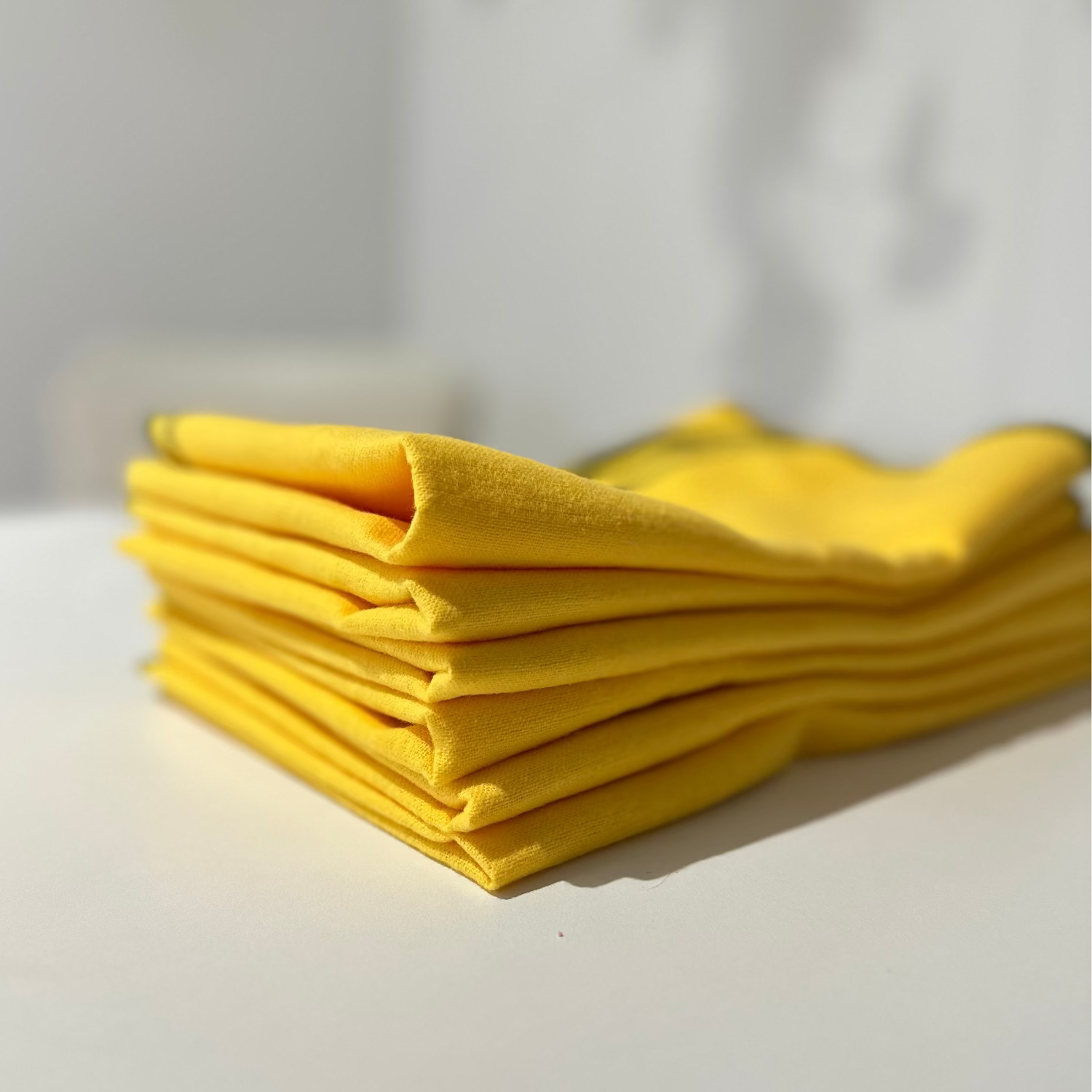 A stack of folded bright yellow cleaning cloths on a white surface with a softly blurred indoor background.